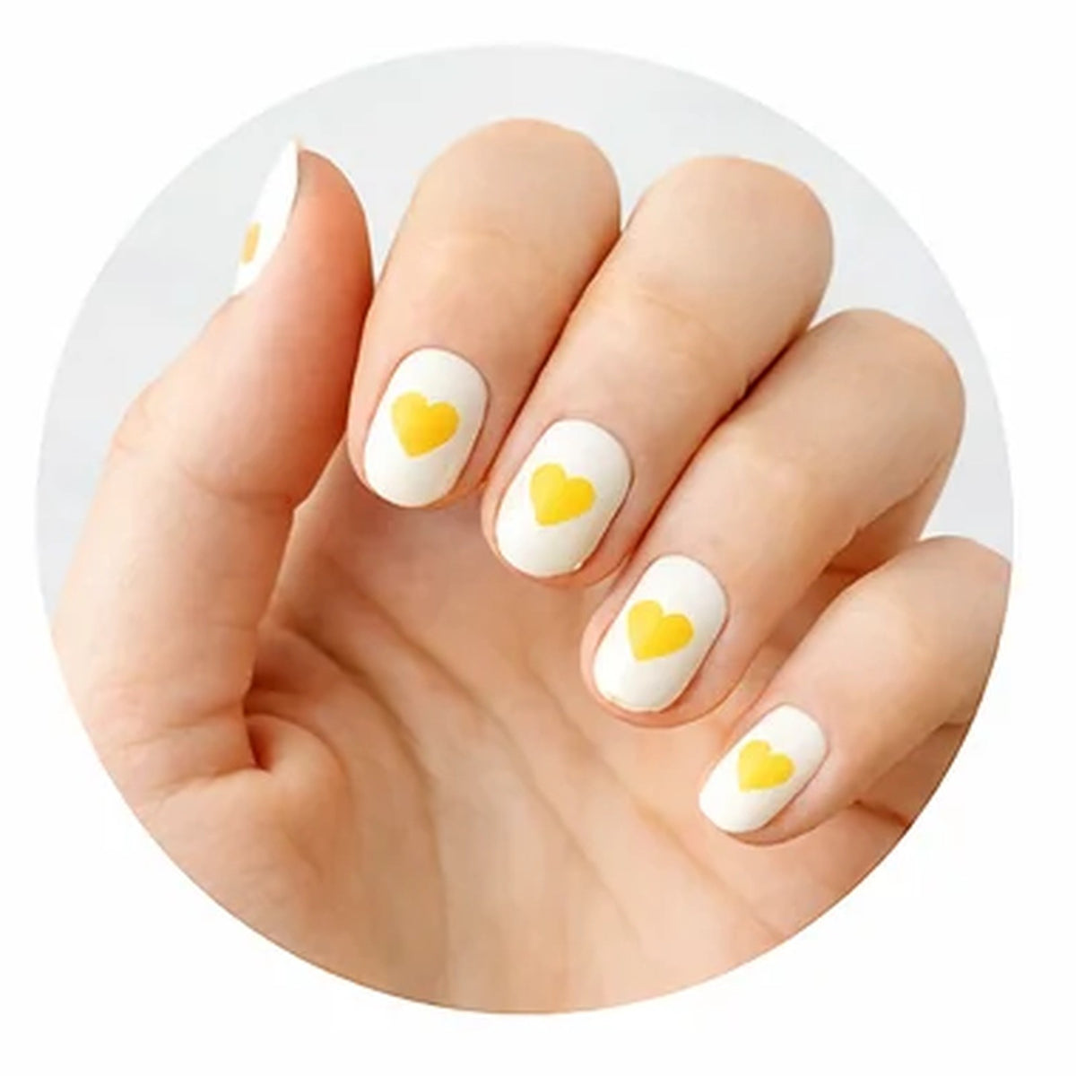 Hand with yellow heart stickers on white-painted nails
